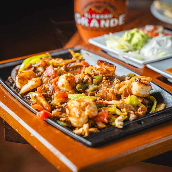 Sizzling shrimp and steak fajitas with peppers and onions, served with sides of guacamole and sour cream.