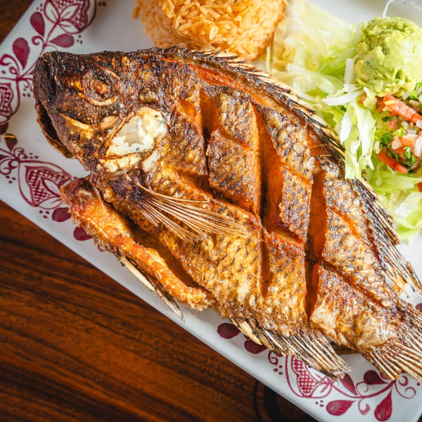 Whole fried fish with rice, lettuce, guacamole, and pico de gallo on a decorative plate.