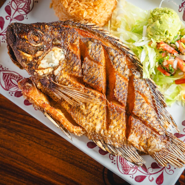 Crispy fried whole fish with rice, guacamole, and pico de gallo on a white plate.
