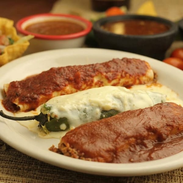 A plate of El Cerro Grande's enchiladas and a chile relleno, with salsa bowls in the background.