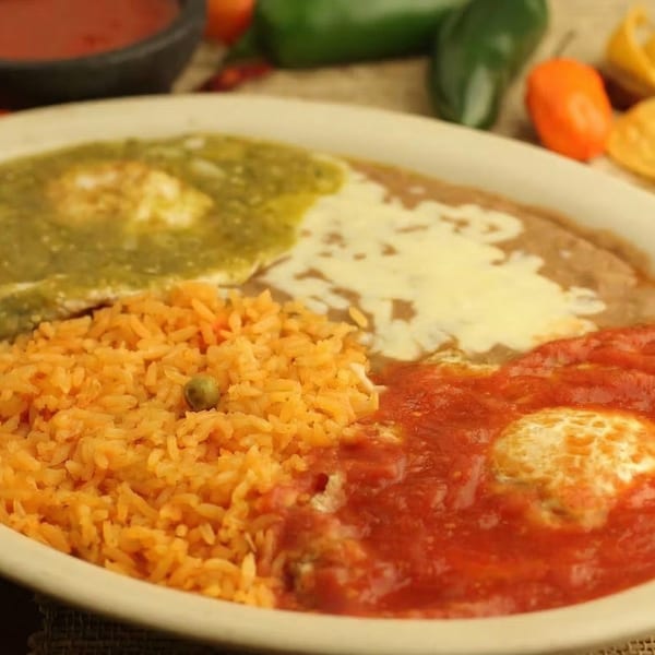 Huevos Rancheros with green and red salsa, refried beans, and Mexican rice on a white plate.
