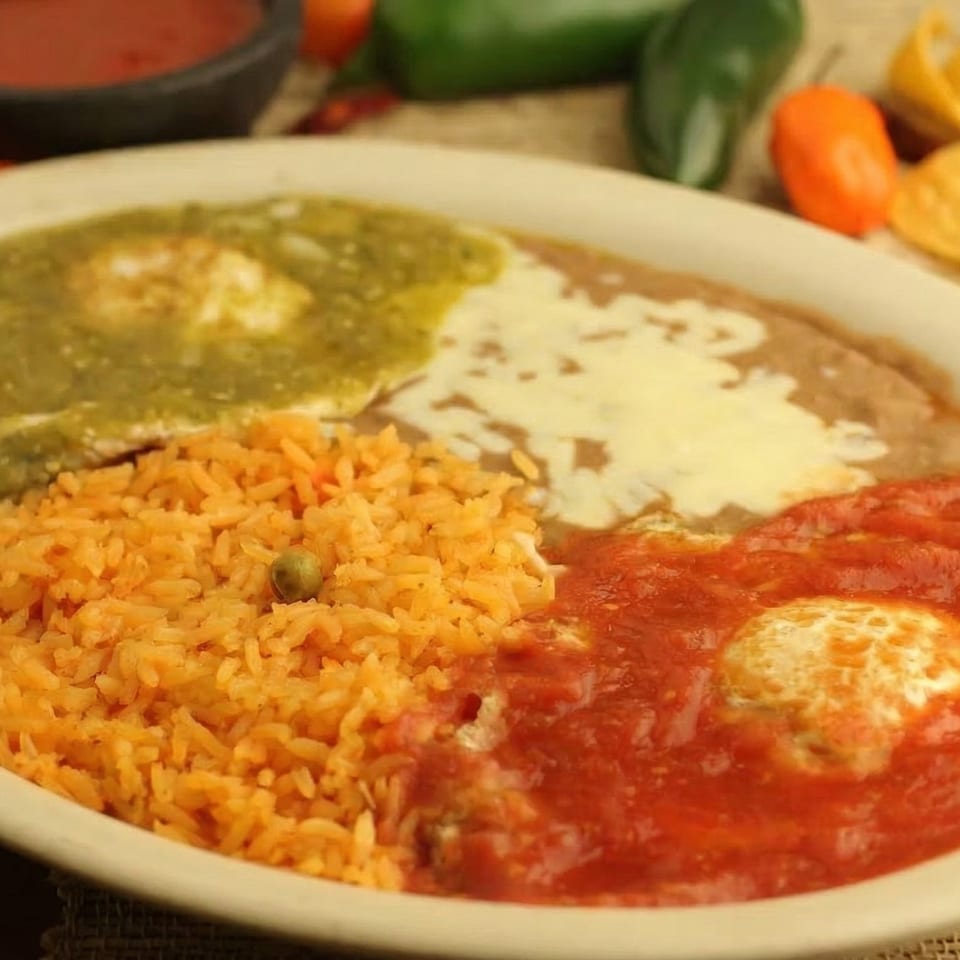 Huevos Rancheros with green and red salsa, refried beans, and Mexican rice on a white plate.