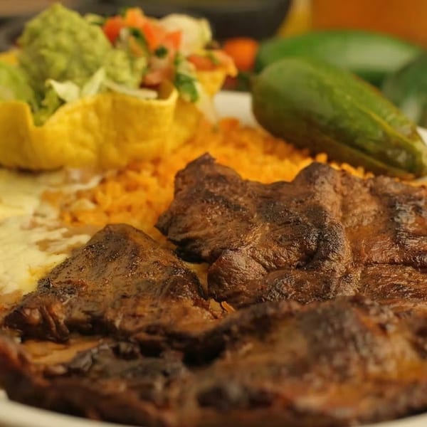 Grilled steak with rice, refried beans, guacamole, and pico de gallo in a tortilla bowl.