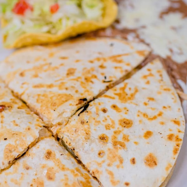 A close-up of a cheese quesadilla cut into wedges, with a taco and refried beans in the background.
