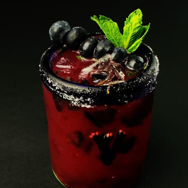 A vibrant red El Cerro Grande margarita, garnished with blueberries and mint, in a sugar-rimmed glass.