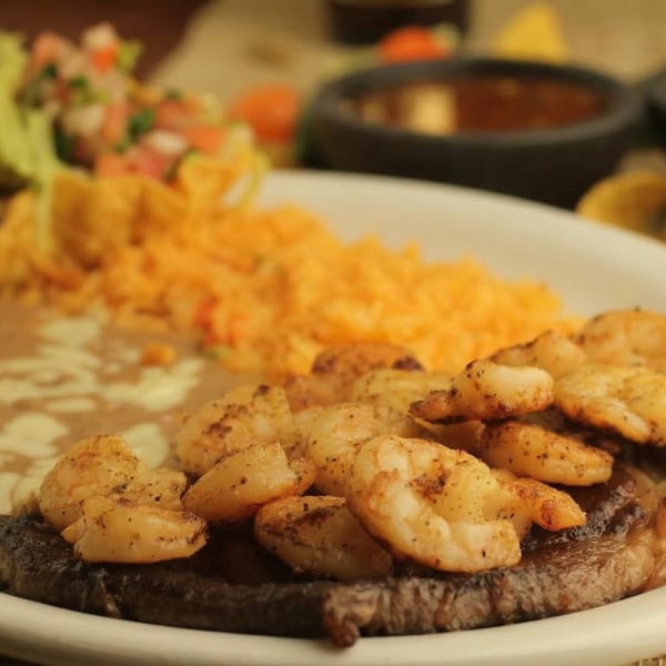 Grilled shrimp and steak with rice, refried beans, and salsa on a white plate at El Cerro Grande.