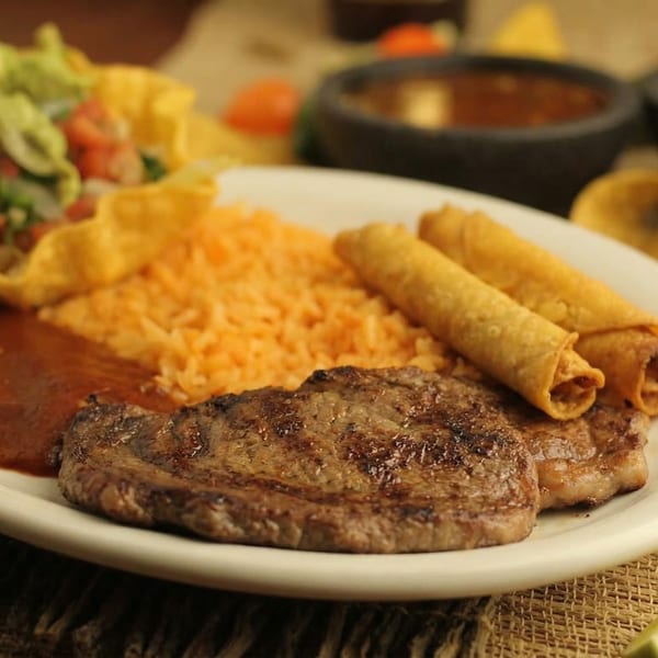 Grilled steak, rice, taquitos, and salad on a white plate at El Cerro Grande.