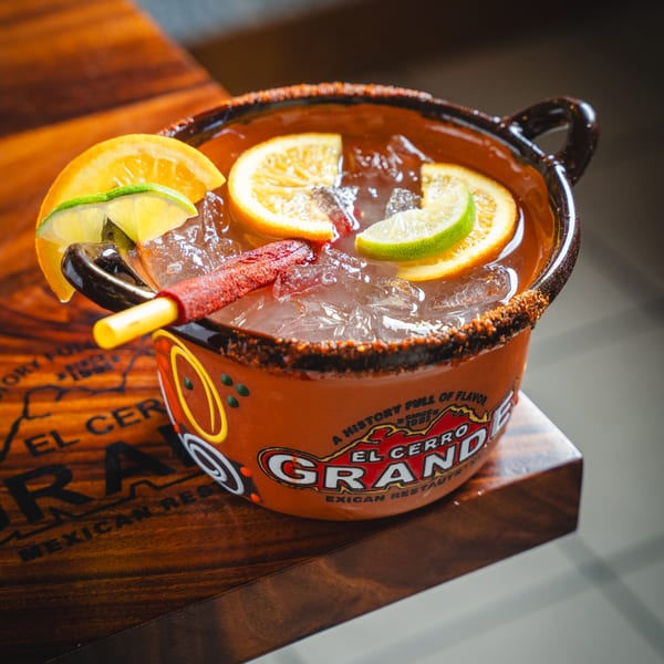 A large El Cerro Grande cocktail with citrus slices and a chili candy straw on a wooden table.