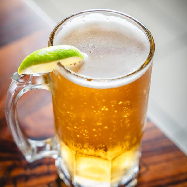Close-up of a frosty mug of golden beer with a lime wedge on a wooden table.