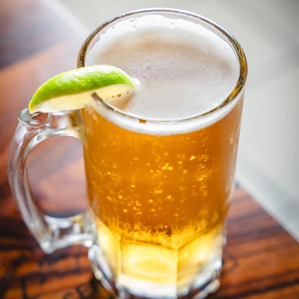 A frosty mug of golden beer with a frothy head and a fresh lime wedge on a wooden table.