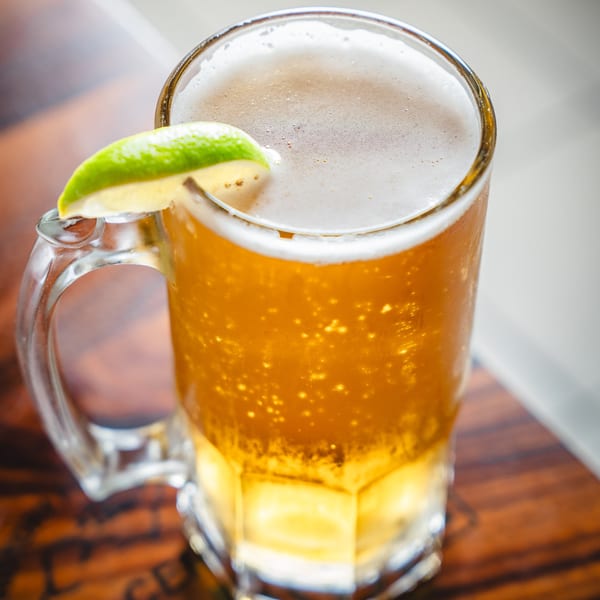 Close-up of a frosty mug of golden beer with a lime wedge on a wooden table.