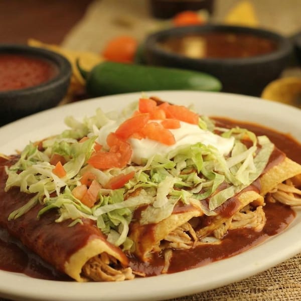 Chicken enchiladas topped with red sauce, shredded lettuce, diced tomatoes, and sour cream.