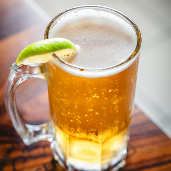 Close-up of a frosty beer mug with a lime wedge on a wooden table.