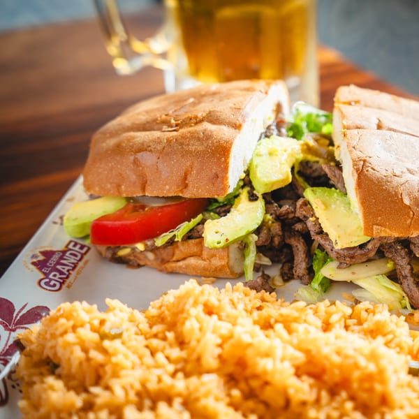 A large El Cerro Grande steak torta with avocado, tomato, and lettuce, served with rice.