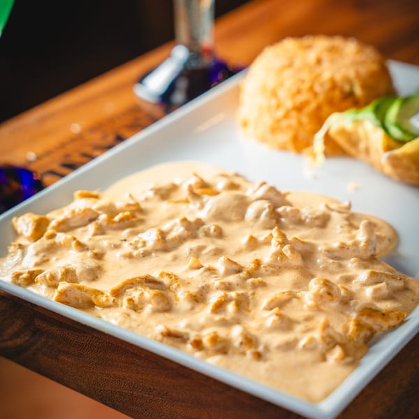 Creamy chicken dish with rice, tortillas, and avocado slices on a white rectangular plate.
