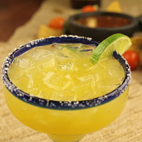 A vibrant yellow margarita with ice and a lime wedge, served in a salt-rimmed glass.