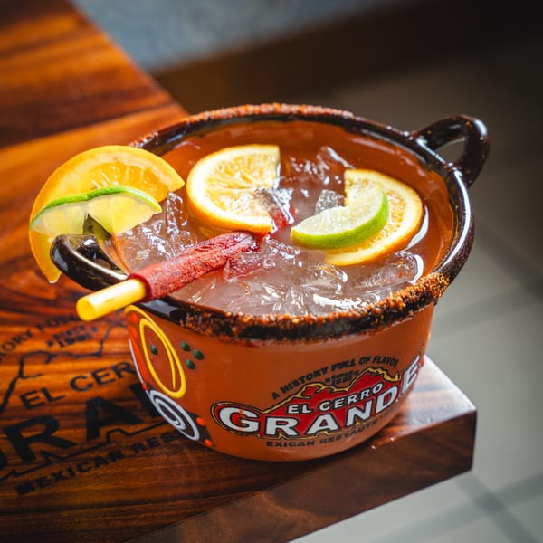 A large El Cerro Grande Mexican Restaurant drink in a clay mug with fruit slices and a candy straw.