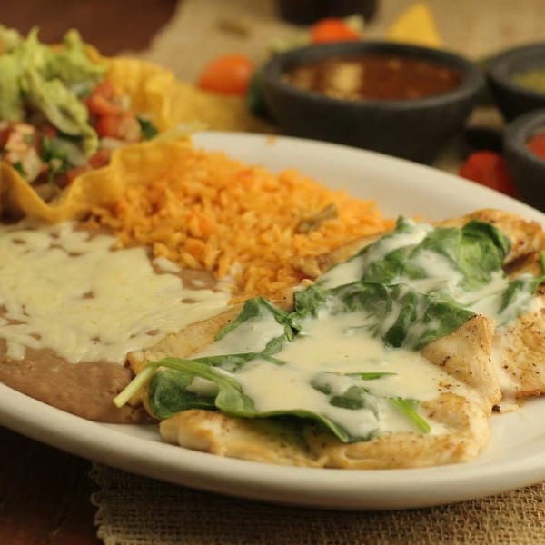 A Mexican dish with chicken, spinach, cheese sauce, refried beans, rice, and a taco salad.
