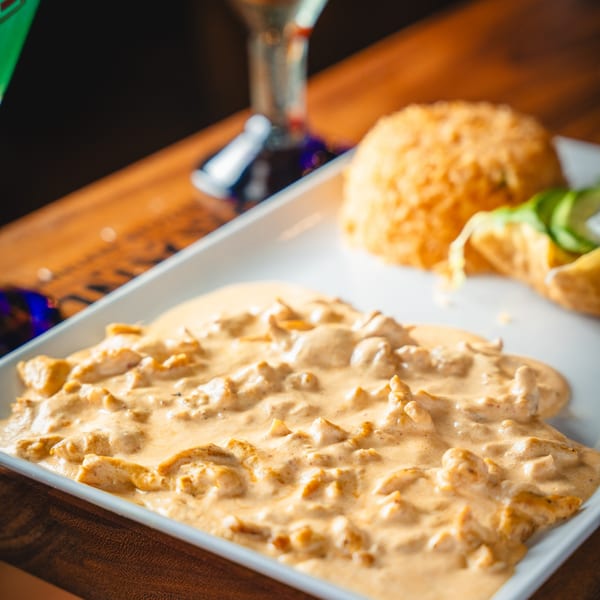 Creamy chicken dish with rice, avocado, and tortilla chips on a white plate.